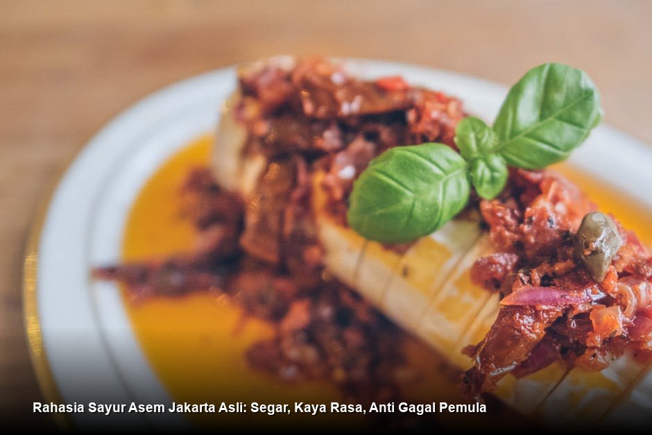 Semangkuk besar Sayur Asem Jakarta yang masih mengepul, menampilkan potongan jagung kuning cerah, labu siam, dan kuah bening kemerahan dengan taburan daun melinjo, disajikan bersama lauk pelengkap.