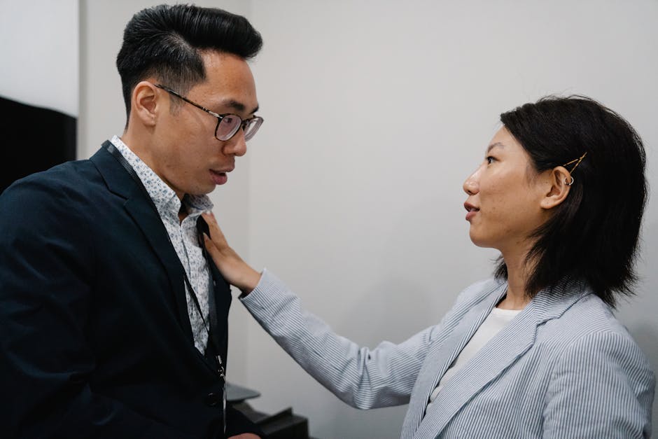 Seorang profesional yang sedang bekerja di laptop sambil tersenyum ke arah pasangannya yang duduk di sofa, menunjukkan keseimbangan antara kerja dan waktu bersama.