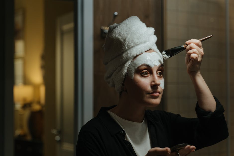 Seorang wanita tersenyum sambil mengaplikasikan produk pelembap pada wajahnya, menunjukkan rutinitas perawatan kulit yang sehat.